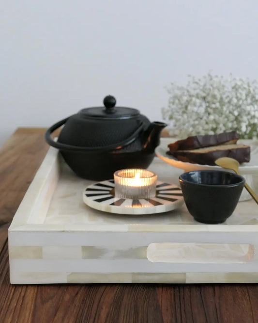 Tea set with black teapot, cup, and candle on a wooden tray.