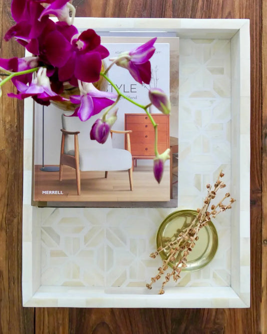 Decorative tray with pink flowers, a magazine, and a small plant on a wooden surface